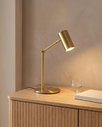 Brushed gold desk lamp with an adjustable arm, on a wooden sideboard