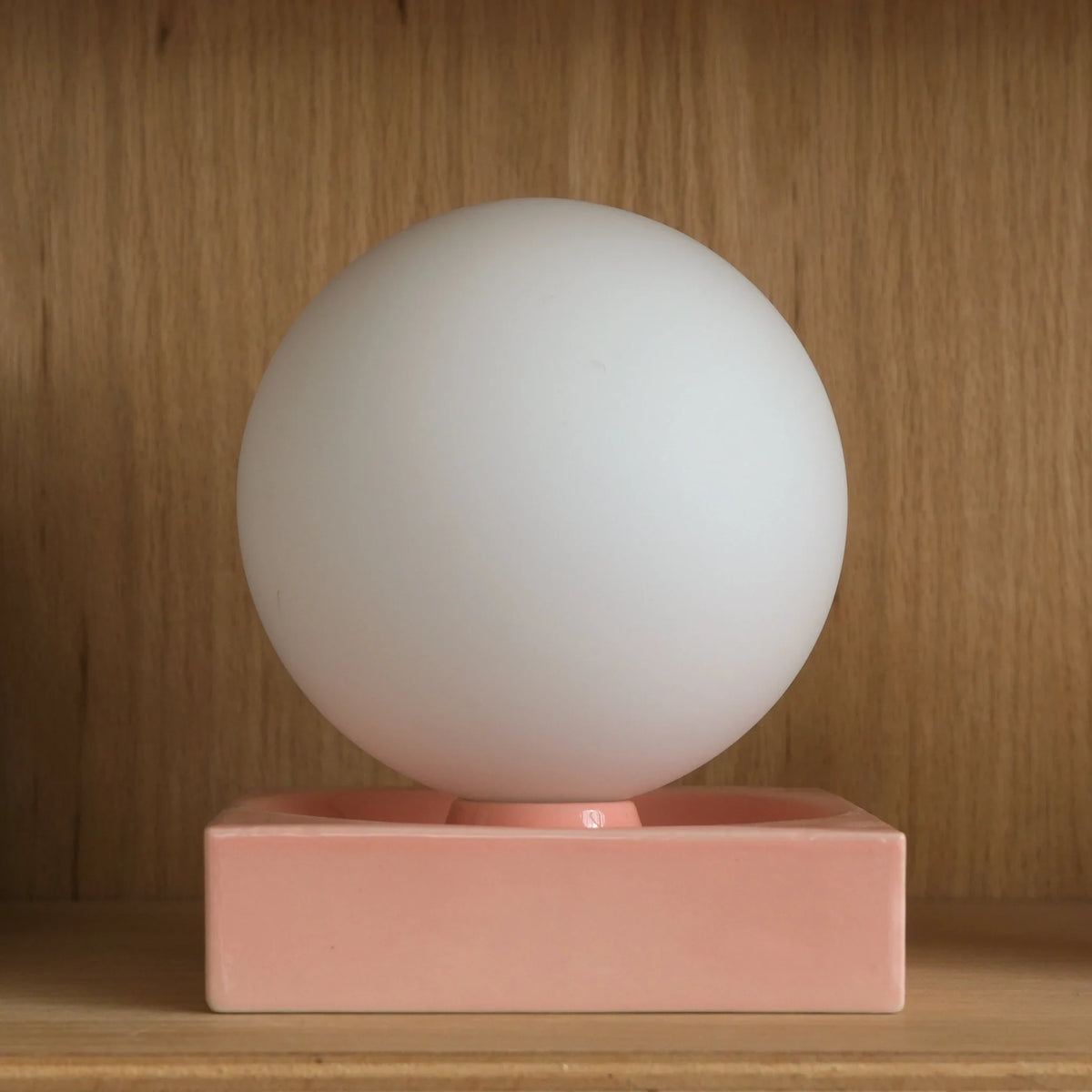 Ceramic cube table lamp with a blown glass globe, in pink on a wooden shelf