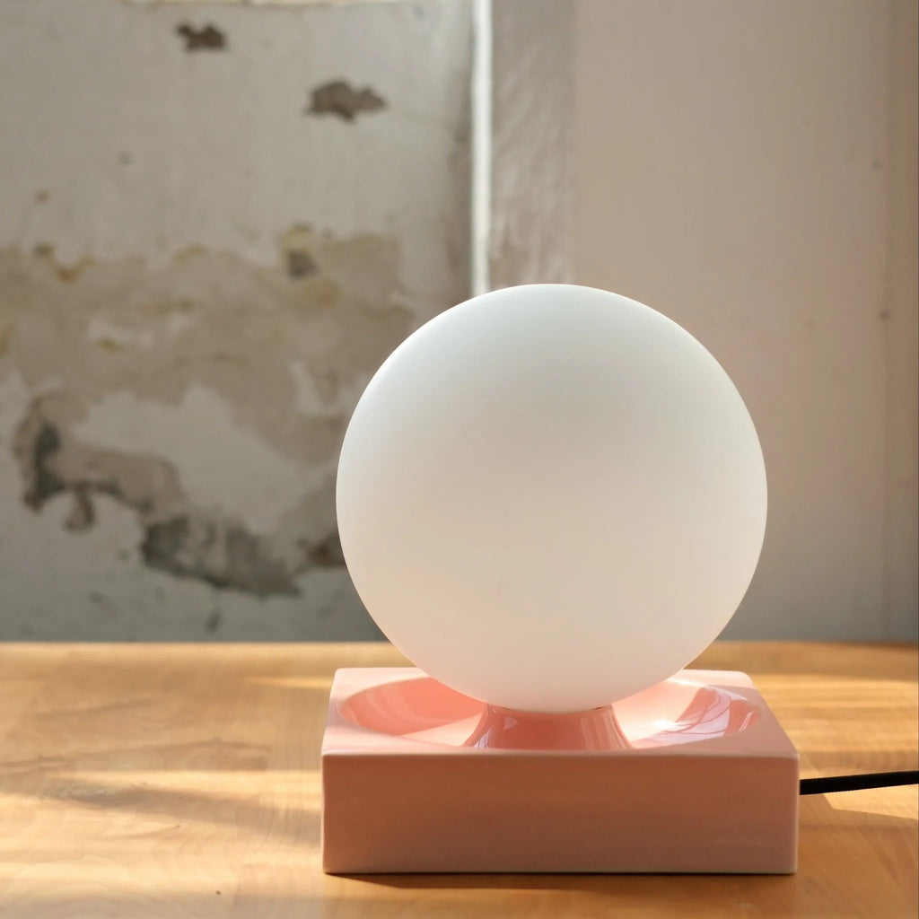 Ceramic cube table lamp with a blown glass globe, in pink, on a shelf