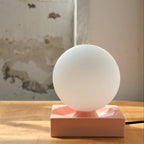 Ceramic cube table lamp with a blown glass globe, in pink, on a shelf