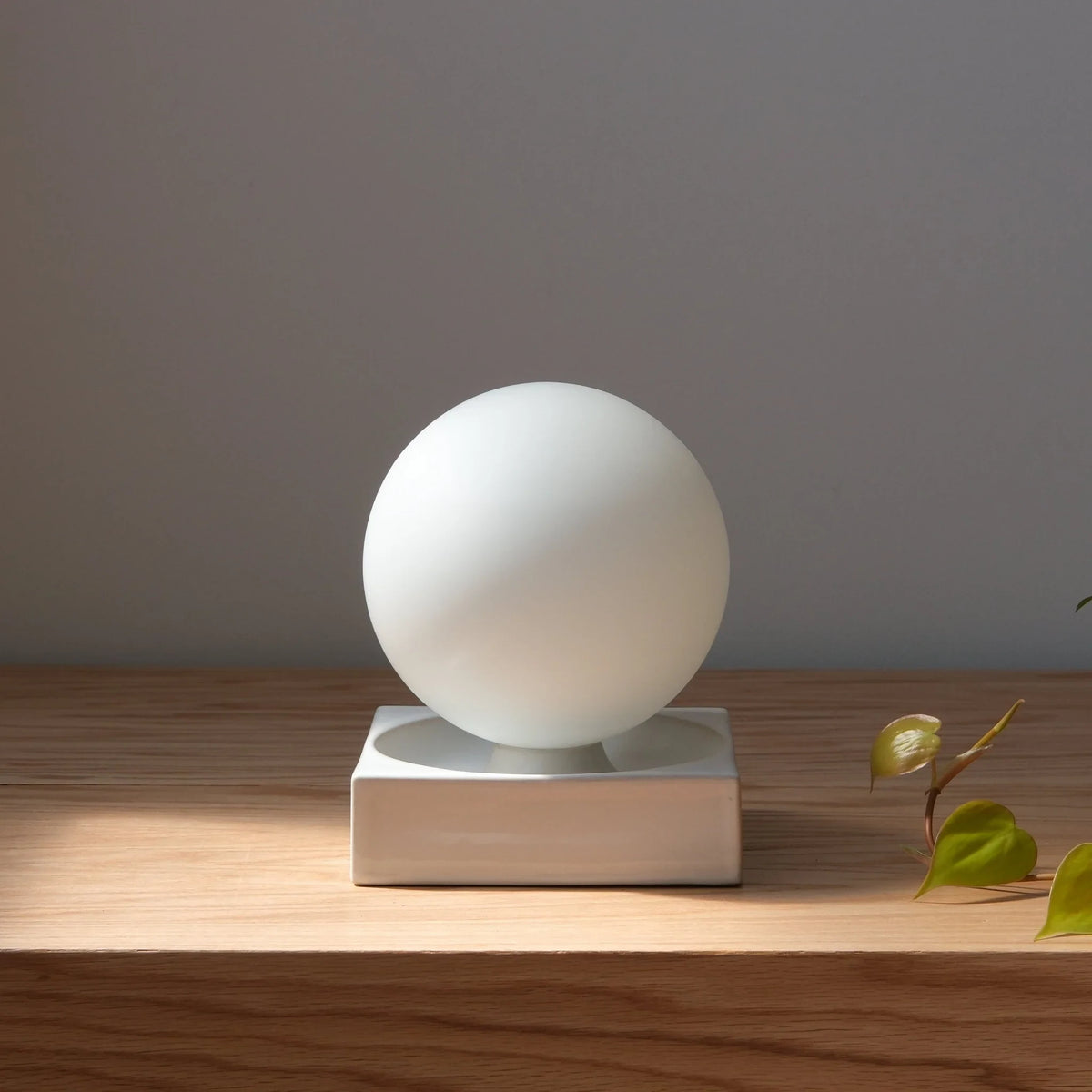 Ceramic cube table lamp with a blown glass globe, in white on a wooden shelf