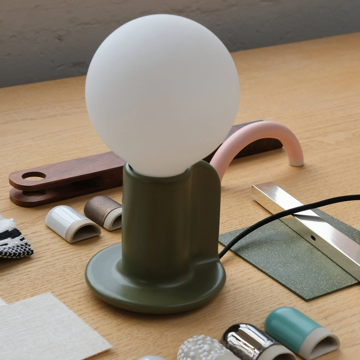 Ceramic table lamp with a paddle handle, in moss beside glaze samples