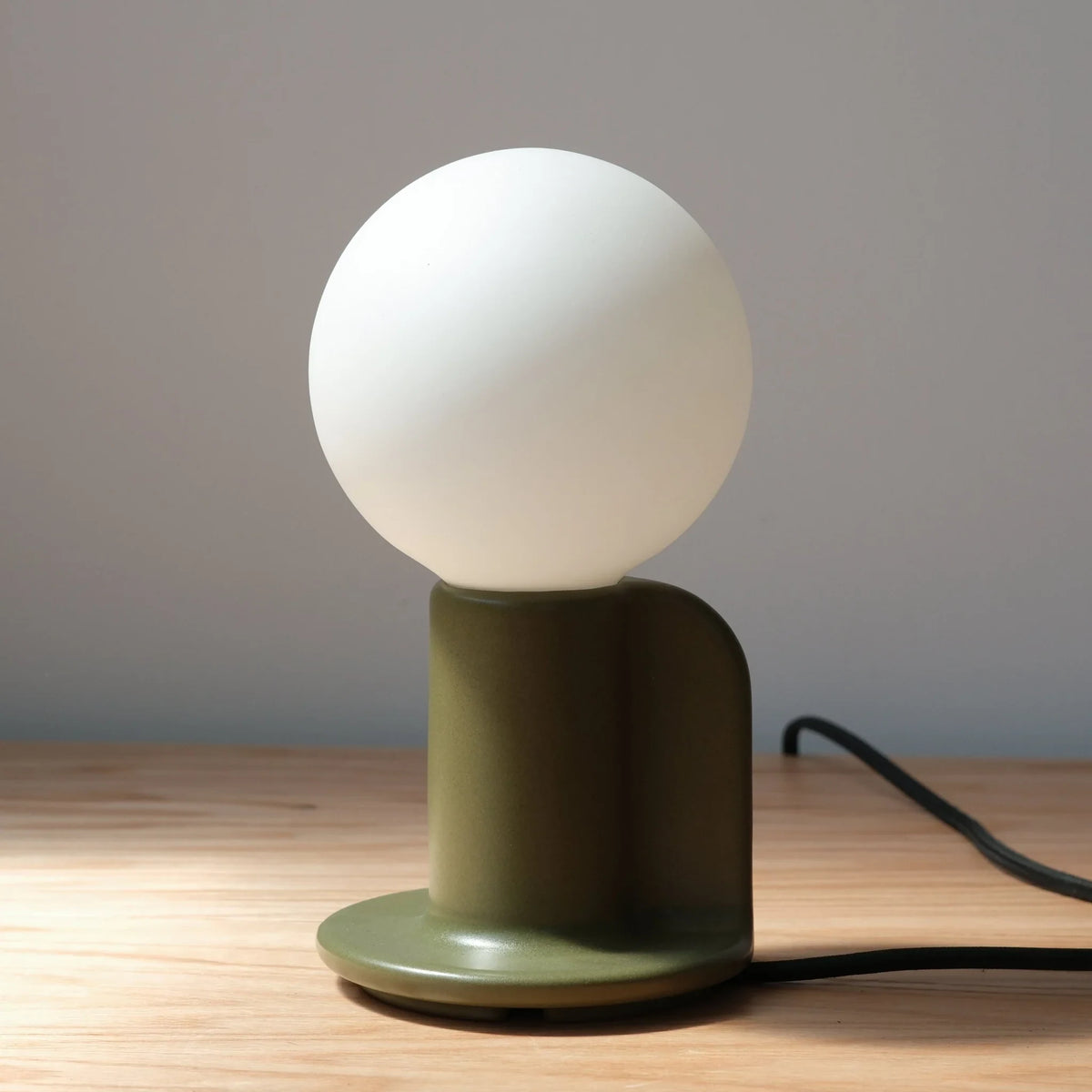 Ceramic table lamp with a paddle handle, in moss, lit