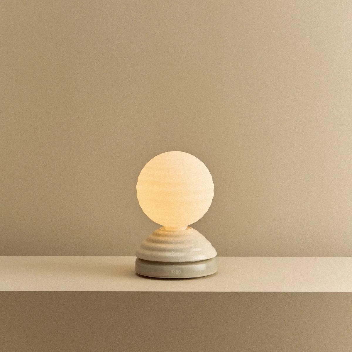 Ceramic wake light table lamp with sleep sounds, pebble white, lit, on a shelf