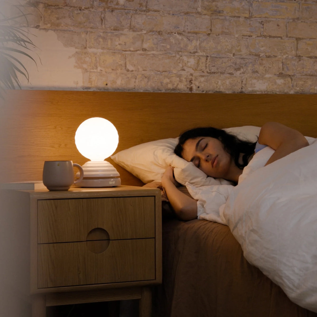 Ceramic wake light table lamp with sleep sounds, pebble white, on a bedside table