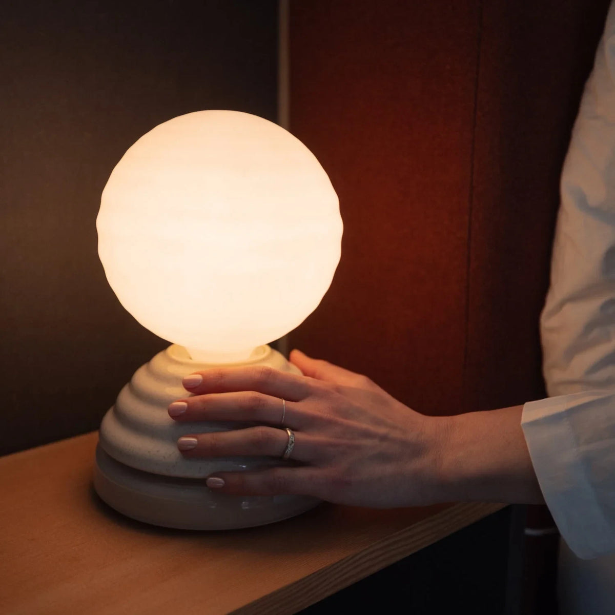 Ceramic wake light table lamp with sleep sounds, pebble white, hand on the rotating base