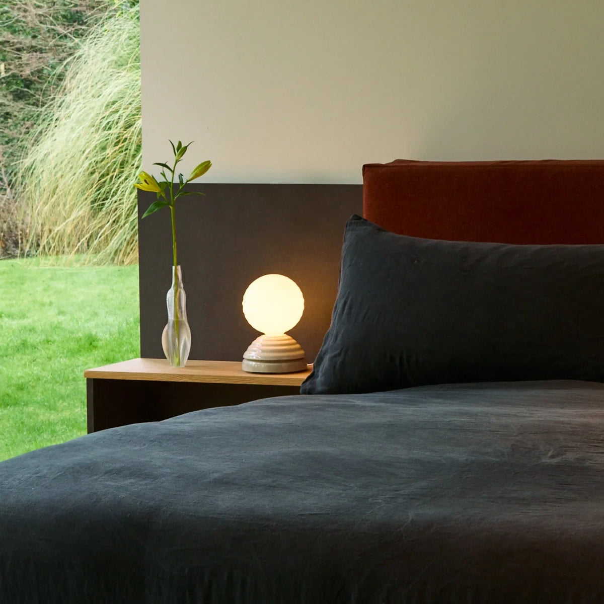 Ceramic wake light table lamp with sleep sounds, pebble white, on a bedside table in a bedroom