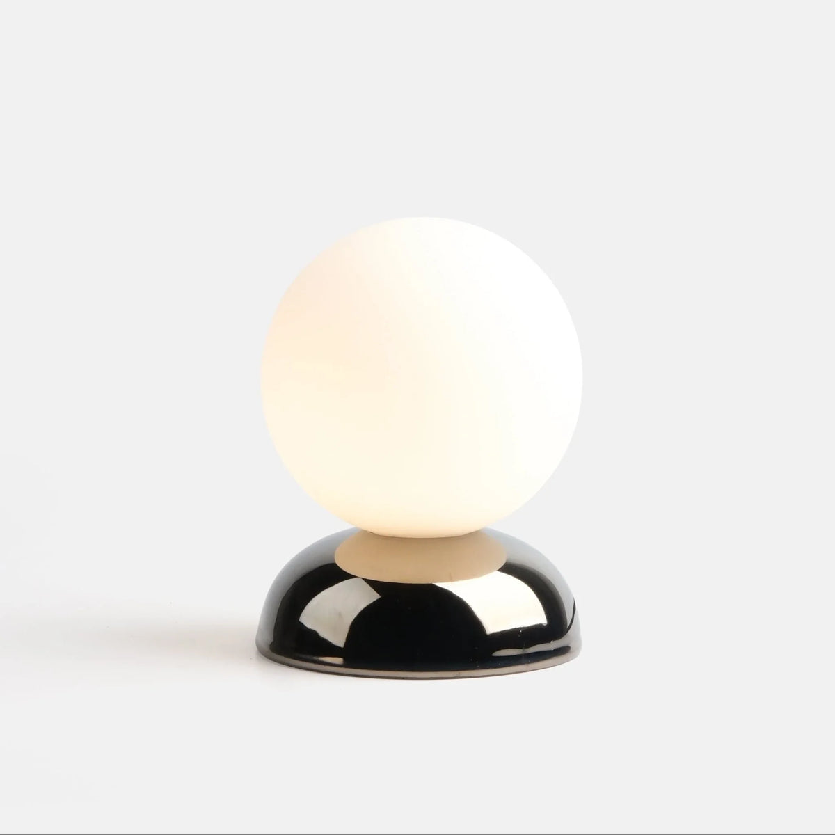 Chrome-glazed rippled table lamp with glass globe, lit, on a plain background