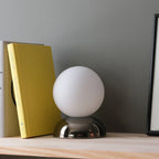Chrome-glazed rippled table lamp with glass globe, on a shelf beside a yellow book