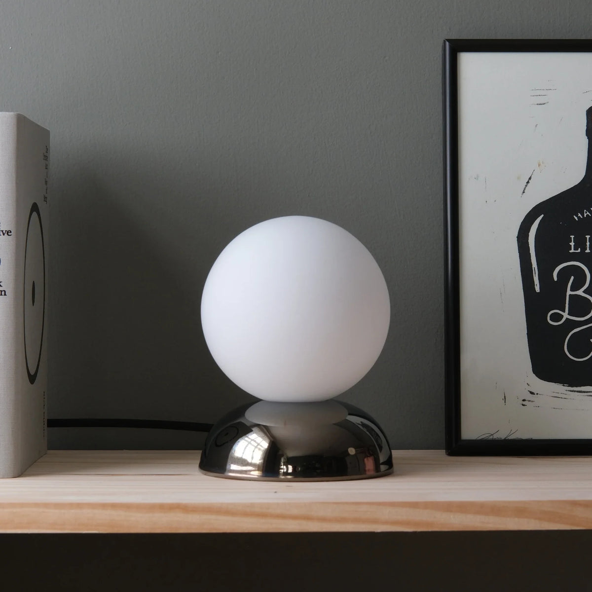 Chrome-glazed rippled table lamp with glass globe, unlit, on a wooden shelf