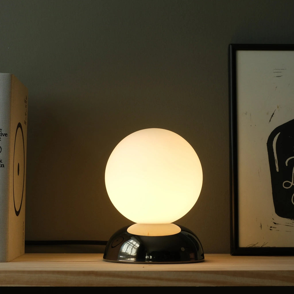Chrome-glazed rippled table lamp with glass globe, lit, beside a framed print