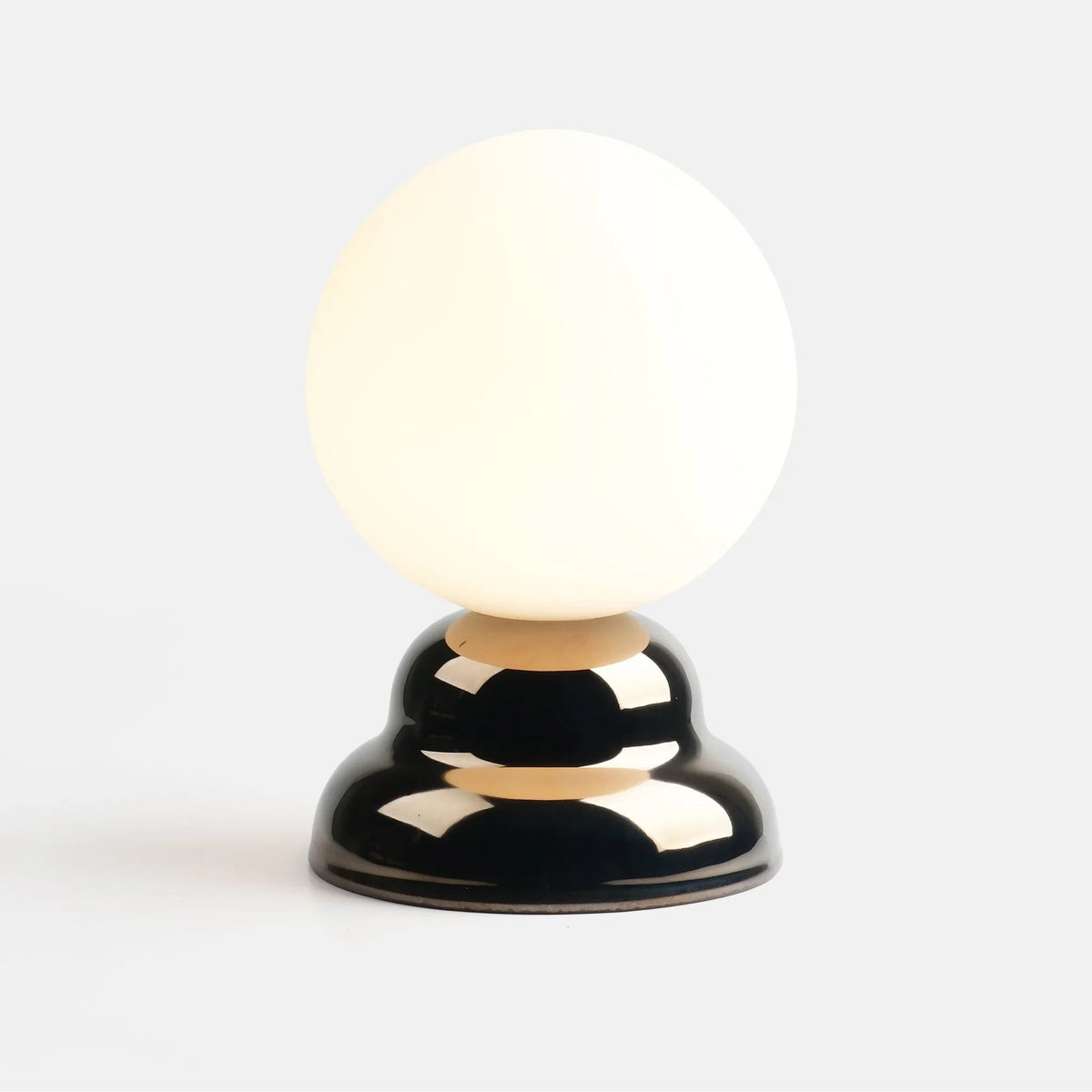 Chrome-glazed rippled table lamp with glass globe, lit, on a plain background