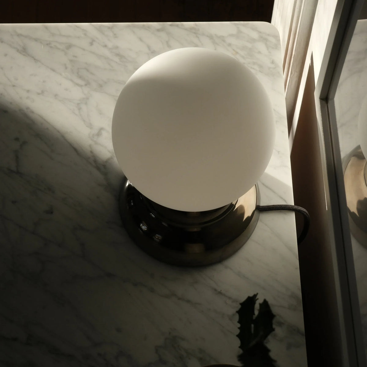Chrome-glazed rippled table lamp with glass globe, on a marble surface by a window