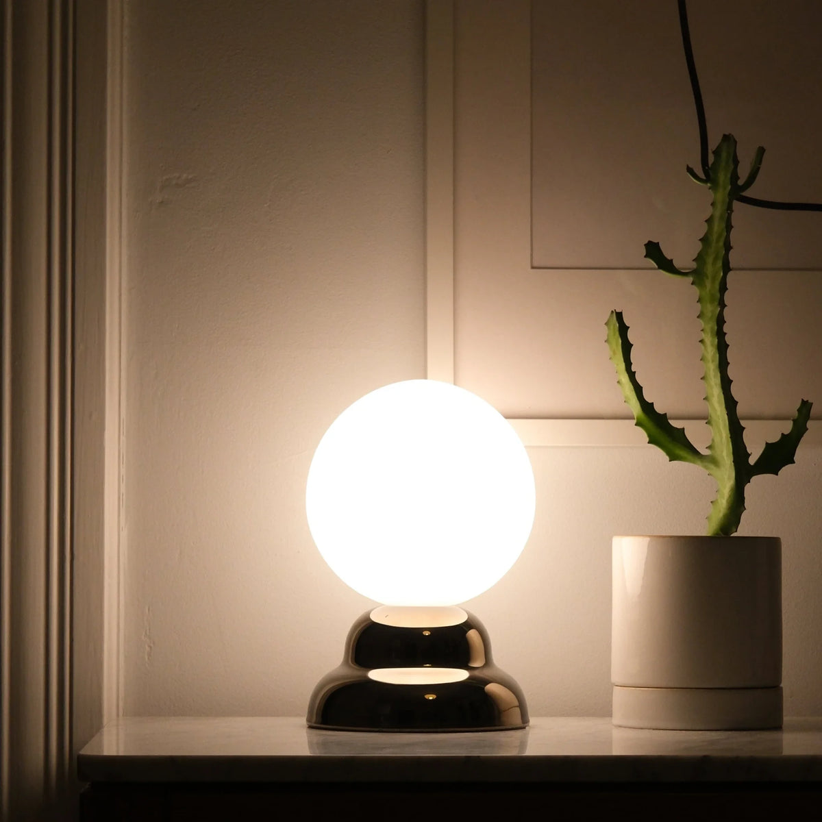 Chrome-glazed rippled table lamp with glass globe, lit, beside a cactus