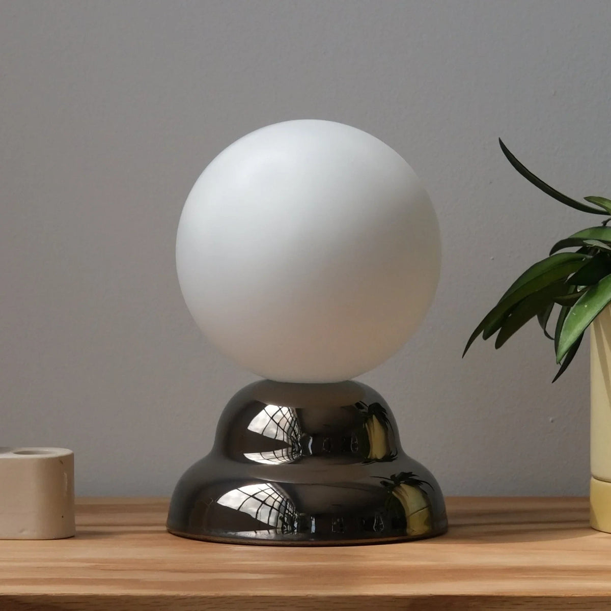 Chrome-glazed rippled table lamp with glass globe, on a wooden surface