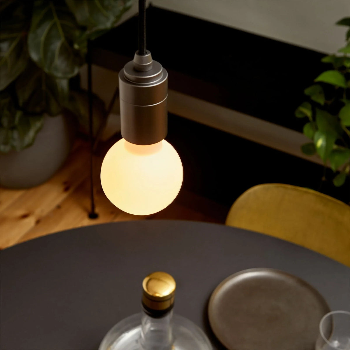Compact opal globe pendant, dim-to-warm, graphite, lit above a dark round table