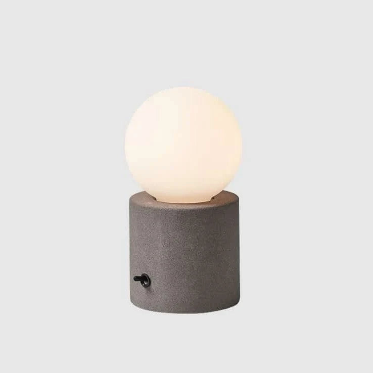 Concrete base table lamp with opal glass globe, lit, on a pale background