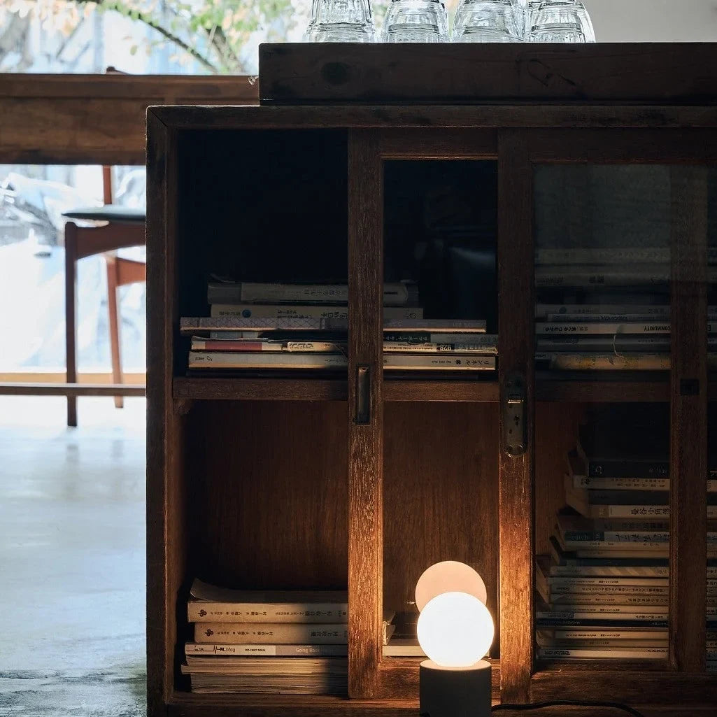 Concrete base table lamp with opal glass globe, lit on the floor in front of a bookcase