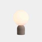 Concrete base table lamp with white glass globe, on a plain background