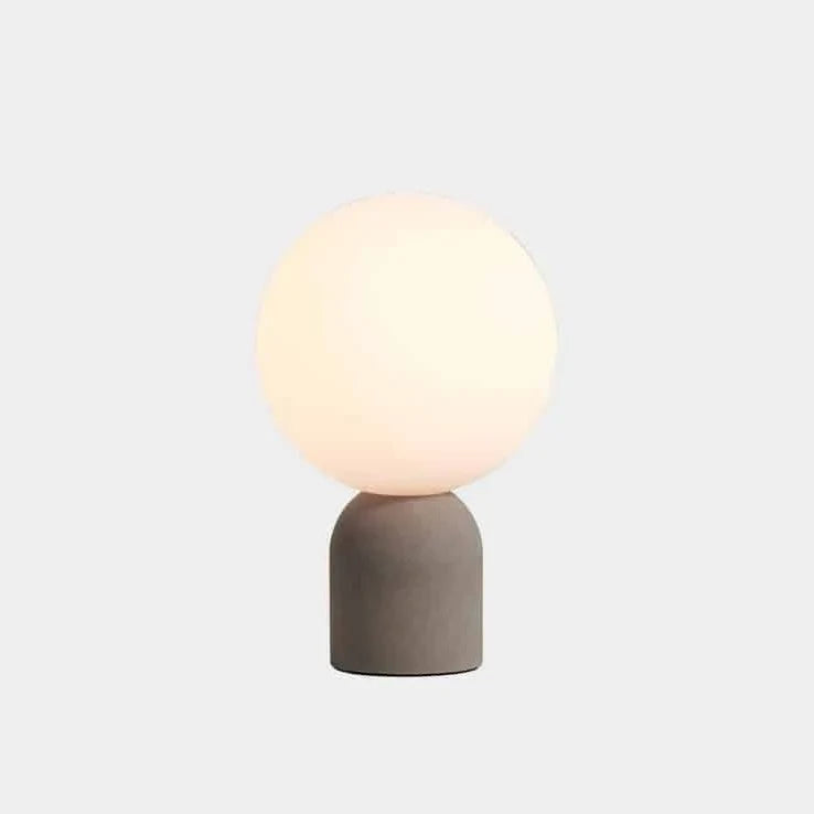 Concrete base table lamp with white glass globe, on a plain background