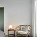 Concrete base table lamp with white glass globe, beside a wicker armchair