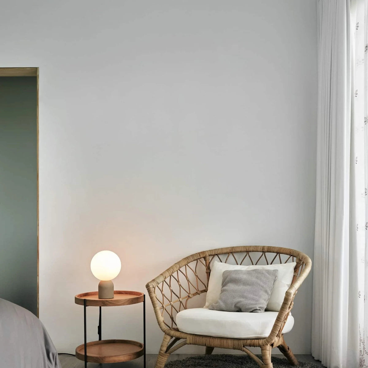 Concrete base table lamp with white glass globe, beside a wicker armchair
