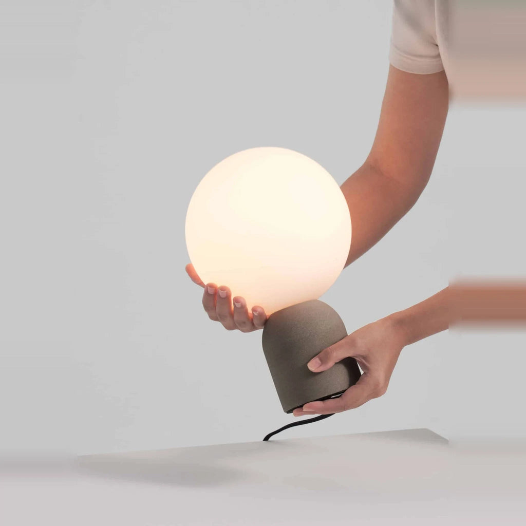 Concrete base table lamp with white glass globe, hand holding the glass globe