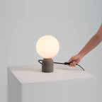 Concrete base table lamp with white glass globe, cable leading to an in-line switch