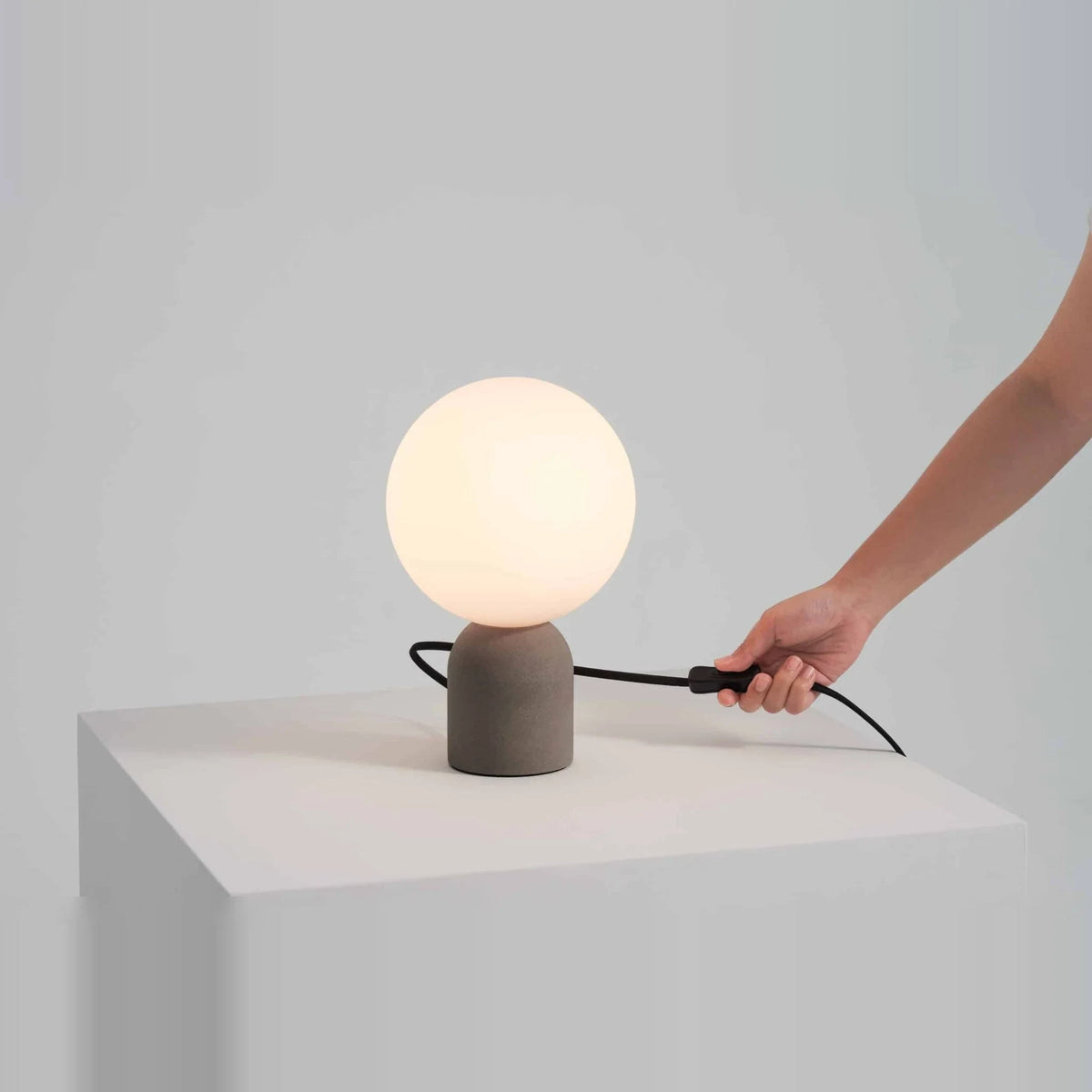 Concrete base table lamp with white glass globe, cable leading to an in-line switch