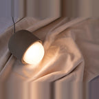 Concrete and opal glass mini pendant, resting on linen, lit
