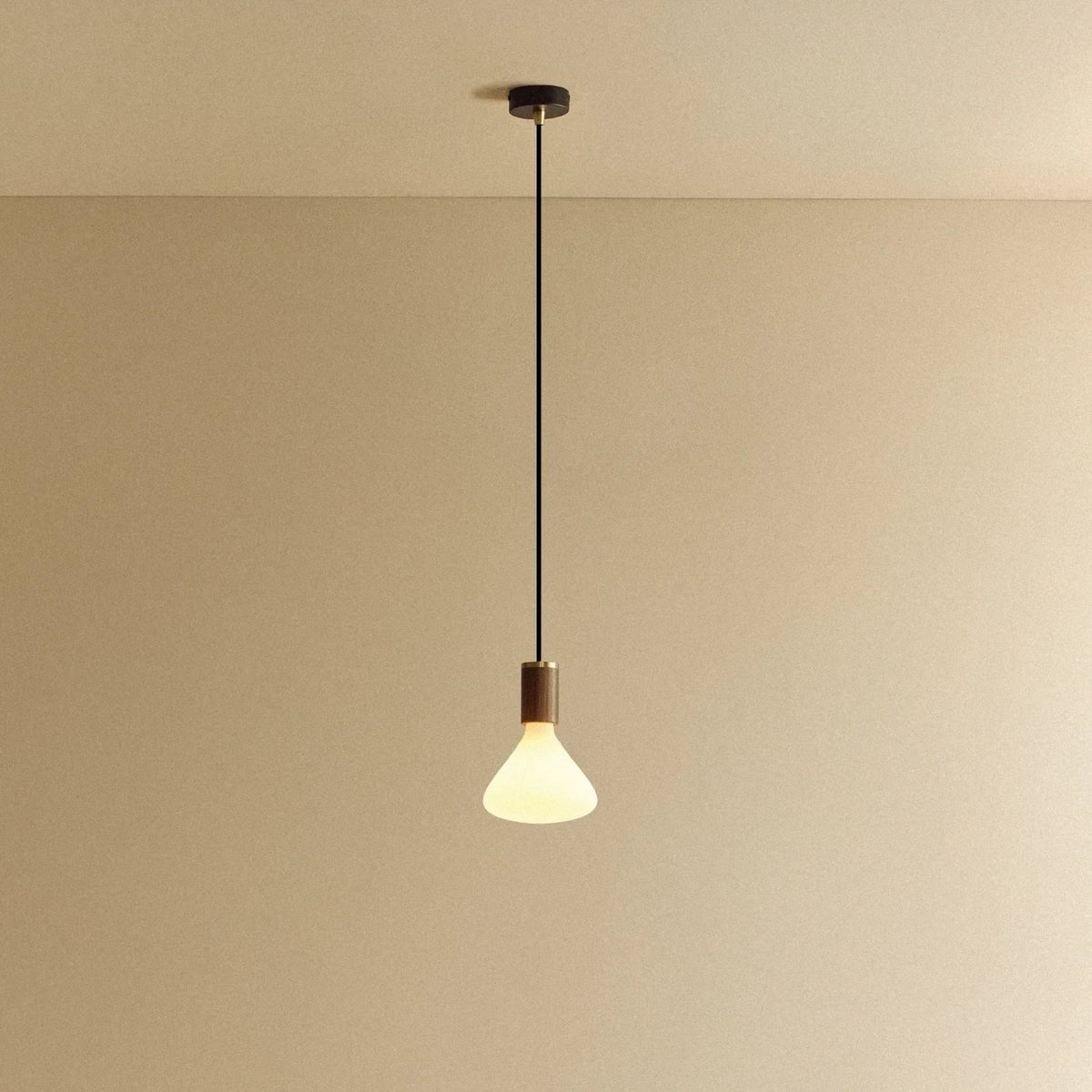 Conical matte white glass pendant, walnut, lit, against a plain wall