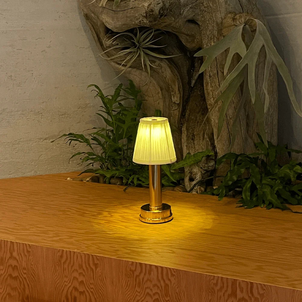 Cordless pleated shade table lamp, lit among plants