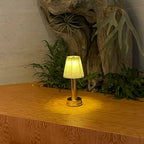 Cordless pleated shade table lamp, lit among plants