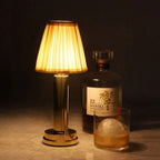 Cordless pleated shade table lamp, lit beside a decanter