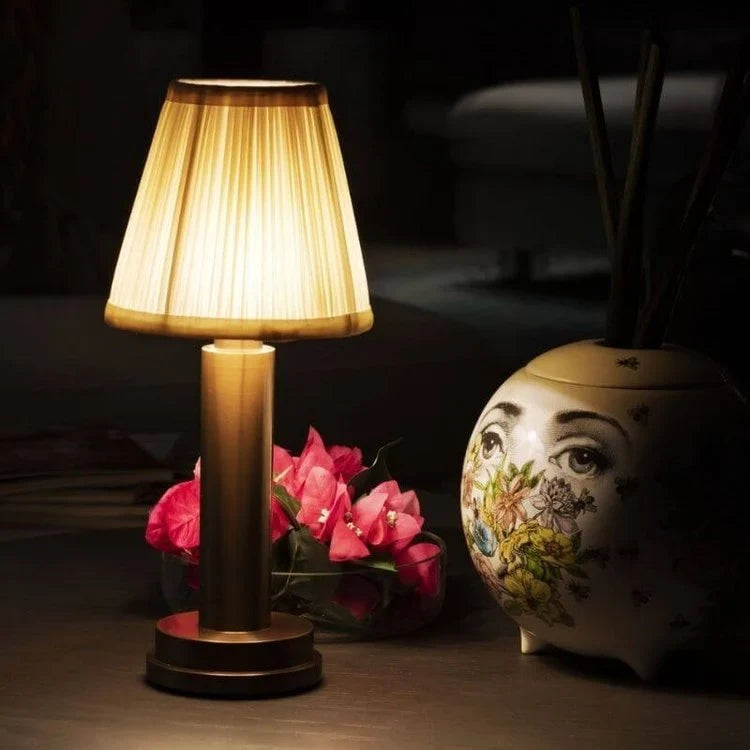 Cordless pleated shade table lamp, lit beside a vase