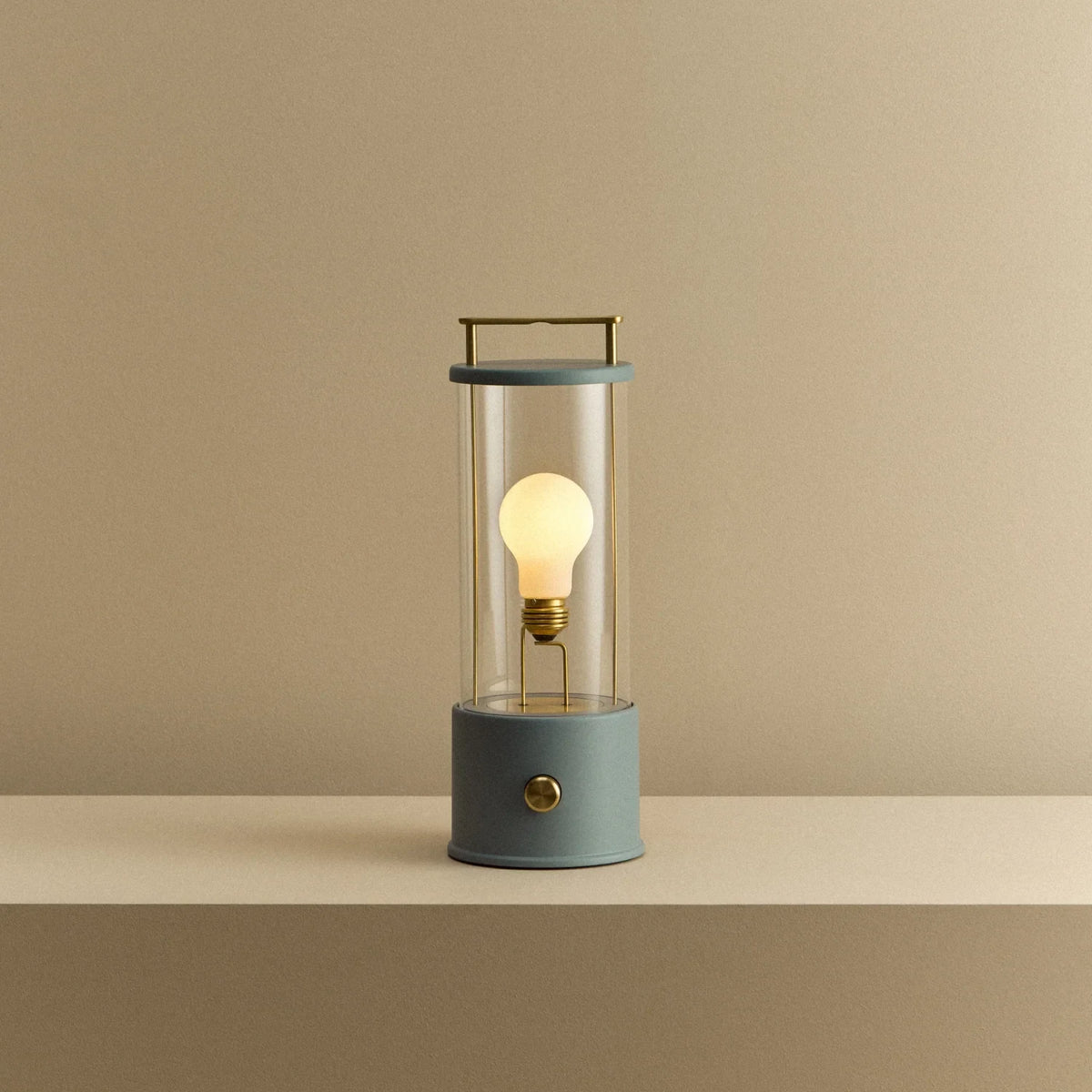 Cordless lantern lamp, blue finish, lit, on a plain ledge