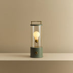 Cordless lantern lamp, green finish, lit, on a plain ledge