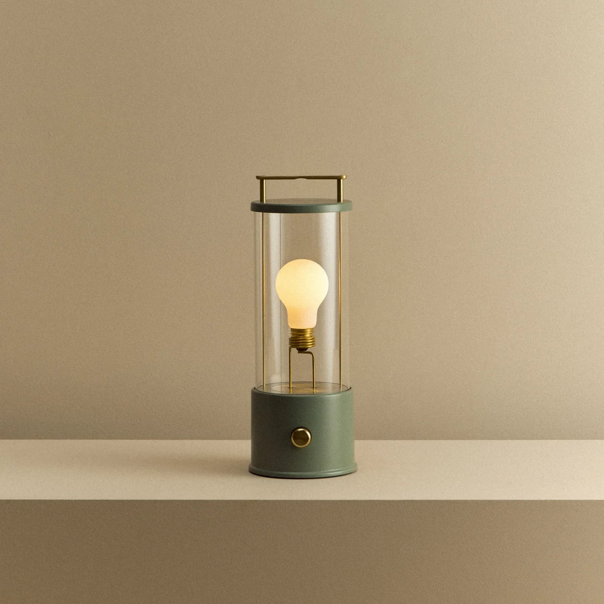 Cordless lantern lamp, green finish, lit, on a plain ledge