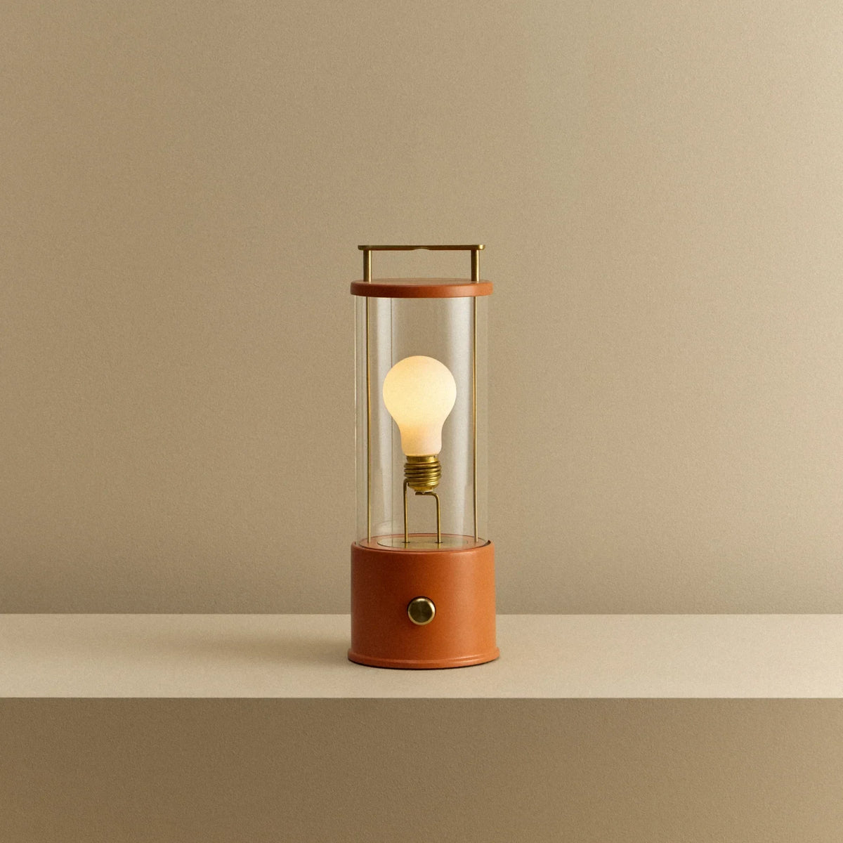 Cordless lantern lamp, orange finish, lit, on a plain ledge