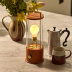 Cordless lantern lamp, orange finish, beside jugs and mugs on a table
