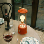 Cordless lantern lamp, orange finish, on a dining table near wine glasses