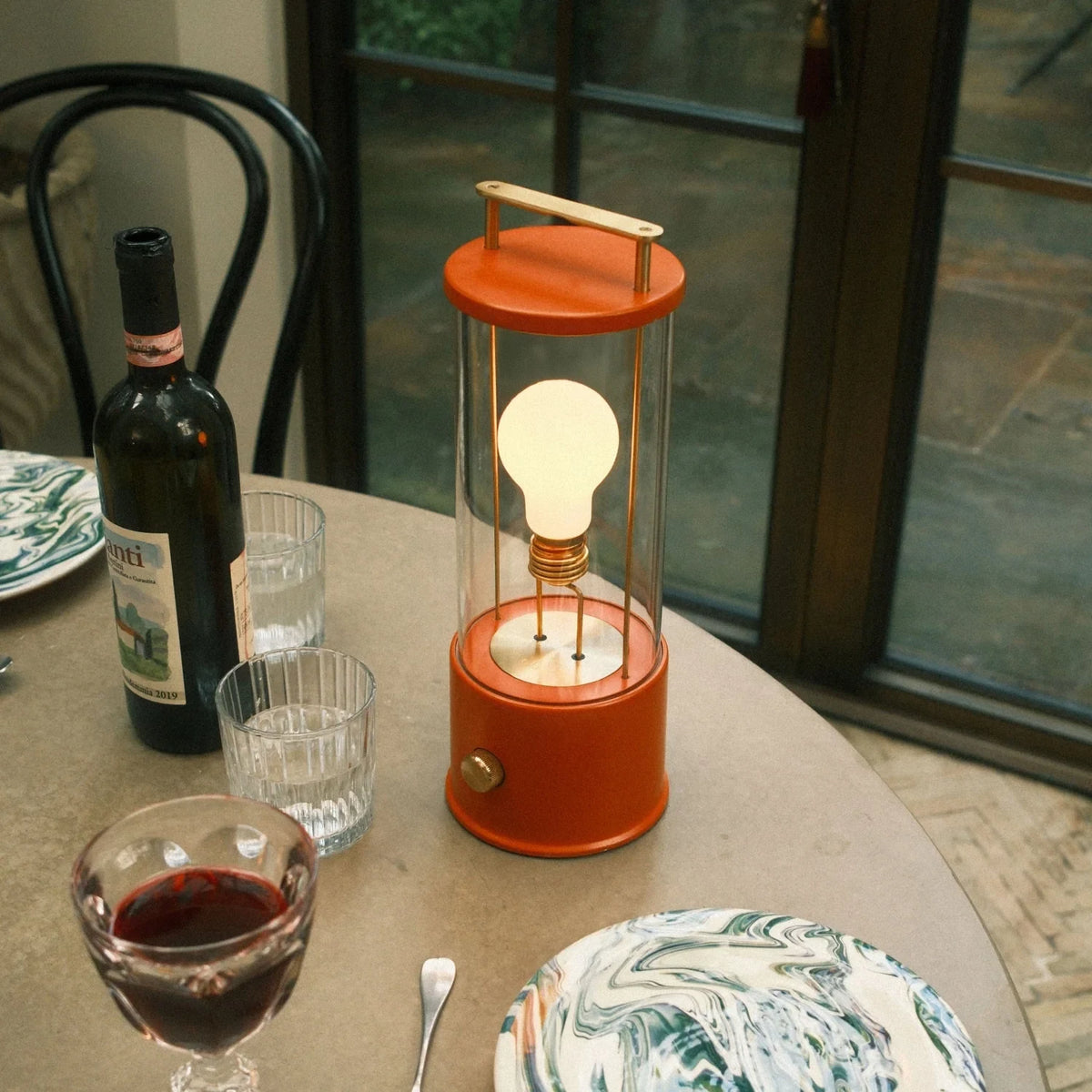 Cordless lantern lamp, orange finish, on a dining table near wine glasses