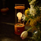 Cordless lantern lamp, orange finish, beside flowers at night