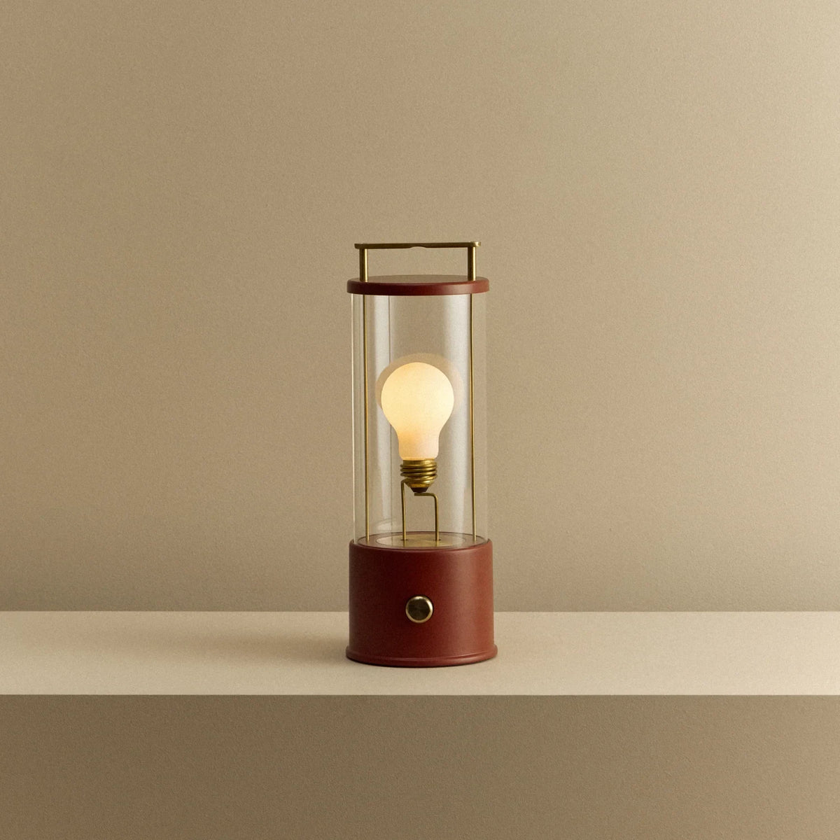 Cordless lantern lamp, red finish, lit, on a plain ledge