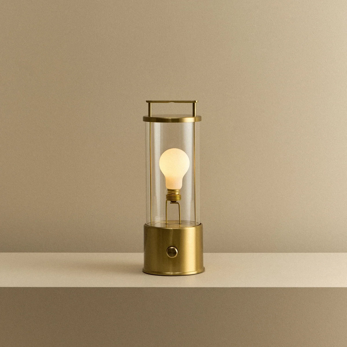 Cordless lantern lamp, solid brass, lit, on a plain ledge