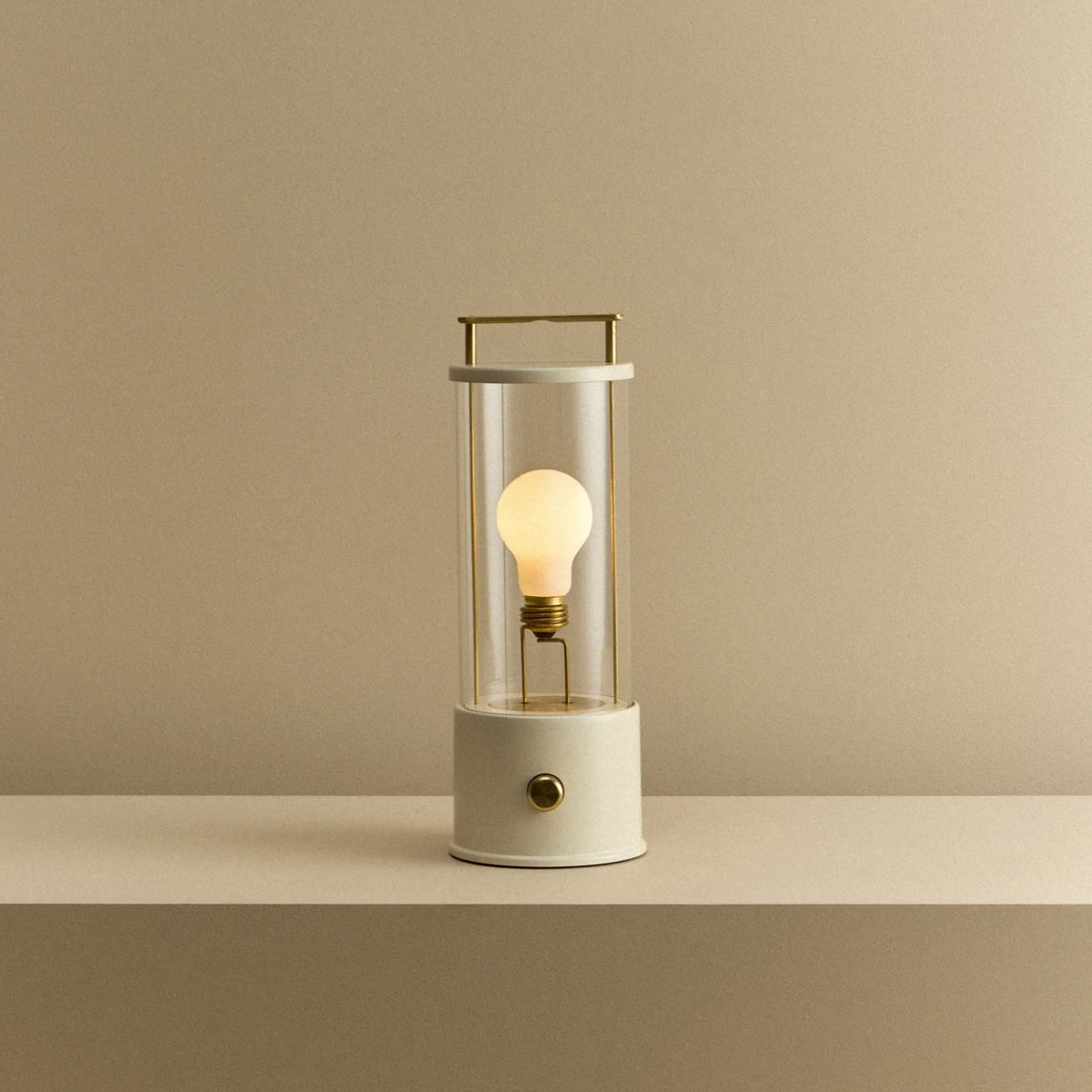 Cordless lantern lamp, white finish, lit, on a plain ledge