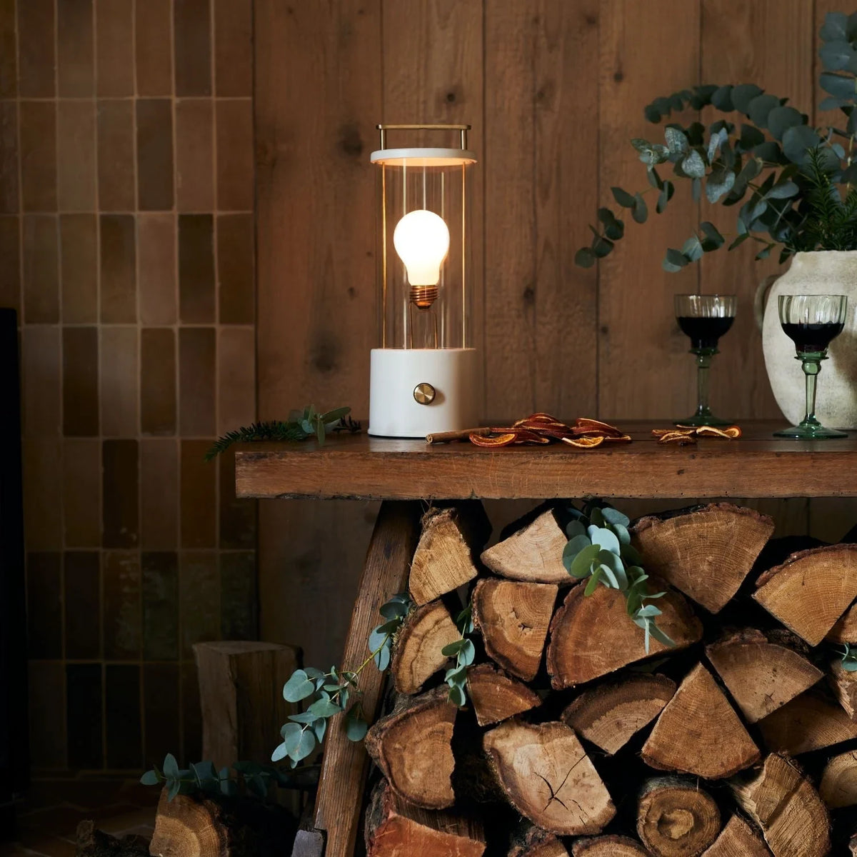 Cordless lantern lamp, white finish, on a shelf above stacked logs