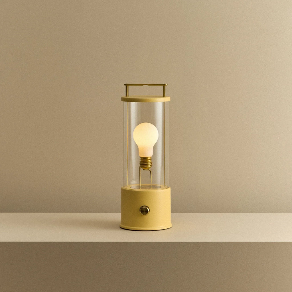 Cordless lantern lamp, yellow finish, lit, on a plain ledge