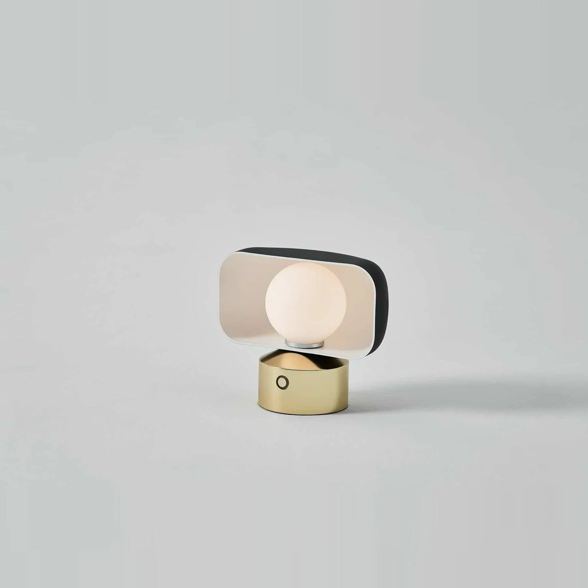 Cordless opal glass table lamp with rotating shade, on a plain wall background