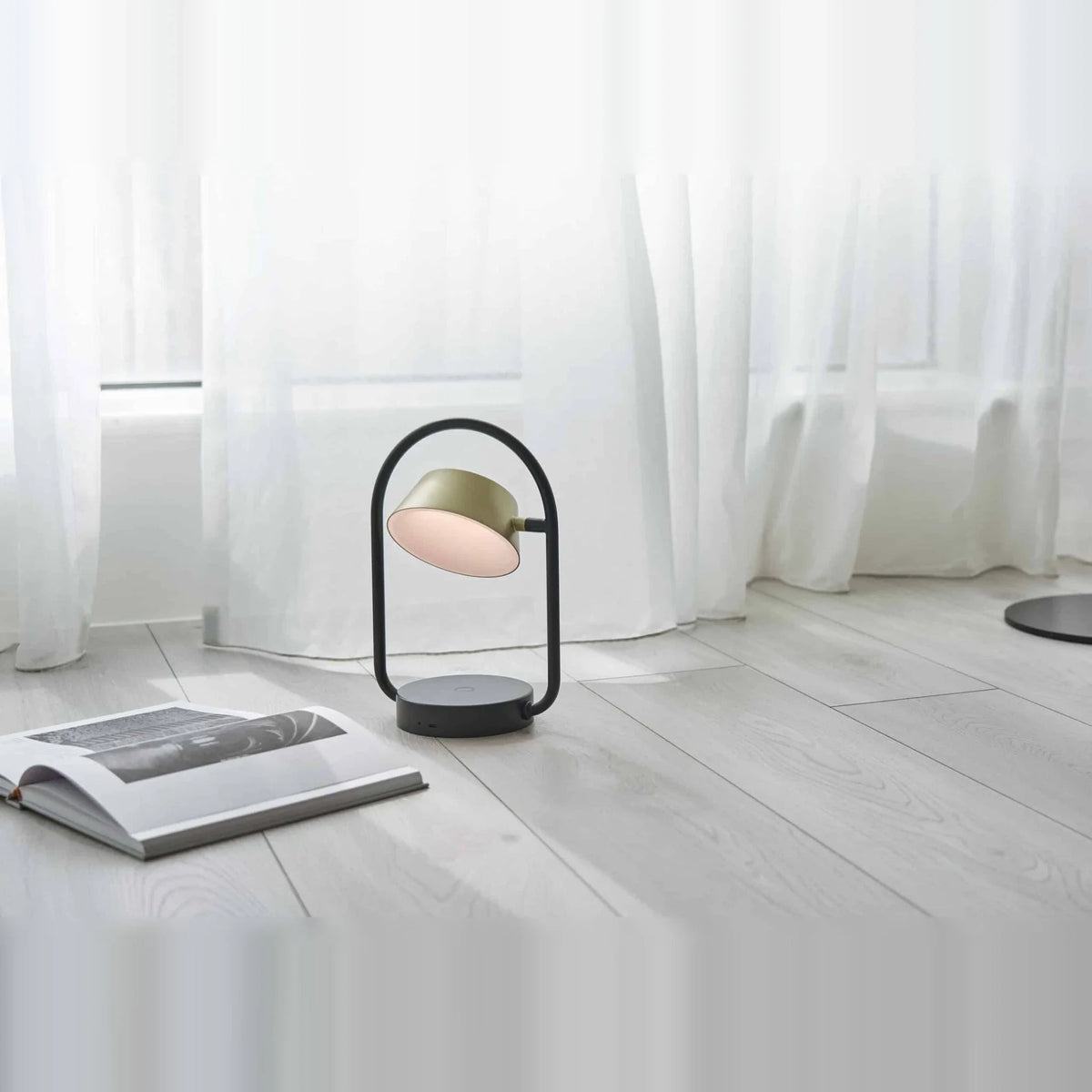 Cordless oval loop table lamp, champagne gold, on a table by sheer curtains